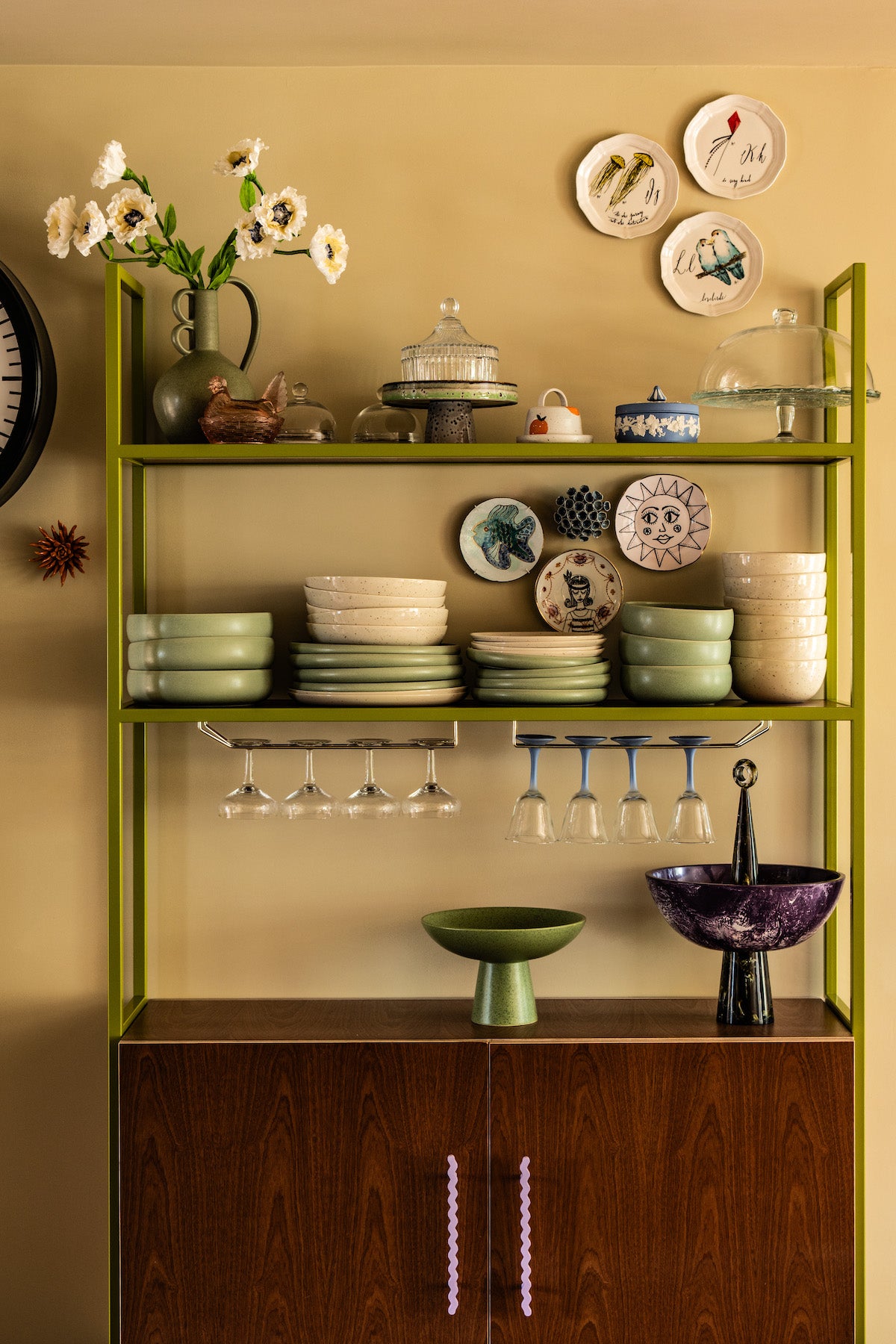Bespoke mid-century style dresser in olive green with sapele wood veneer doors and purple wavy handles, displaying cocktail glasses, plates, flowers, and ornaments.