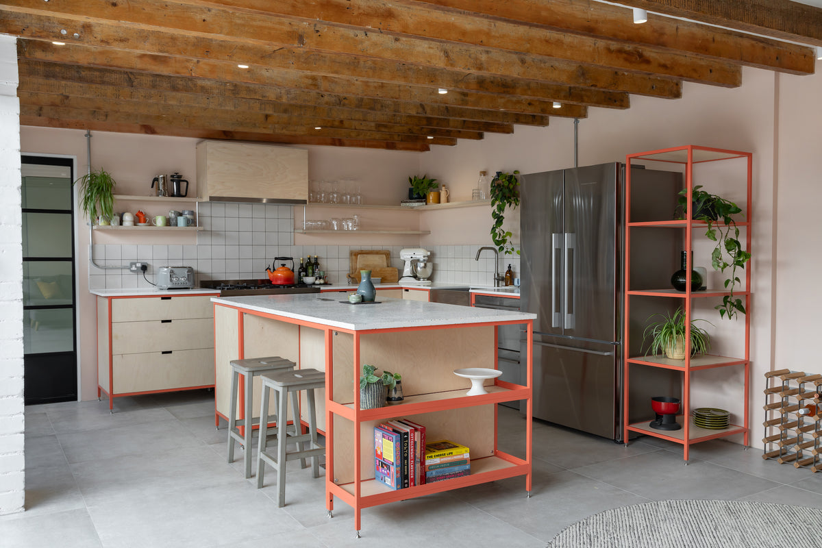 Bespoke steel frame kitchen in powder-coated pink with birch plywood fronts and stainless steel appliances, in a renovated loft with exposed rustic beams.