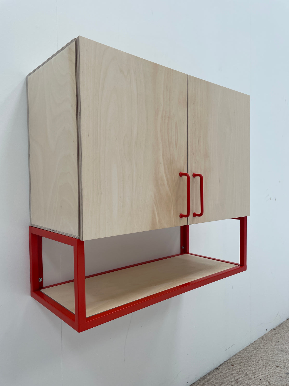 A wall-mounted two-door cabinet with light natural wood doors and a red metal frame base.