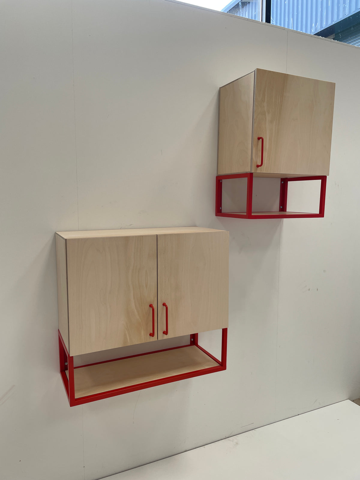Two wall-mounted cabinets with light natural wood doors and red metal frames.