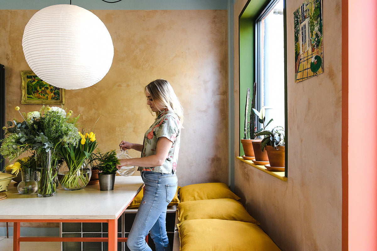 The kitchen dining area with its beige plastered walls, paper lantern lights from HAY, yellow cushions and cati and glass brick built in seating 