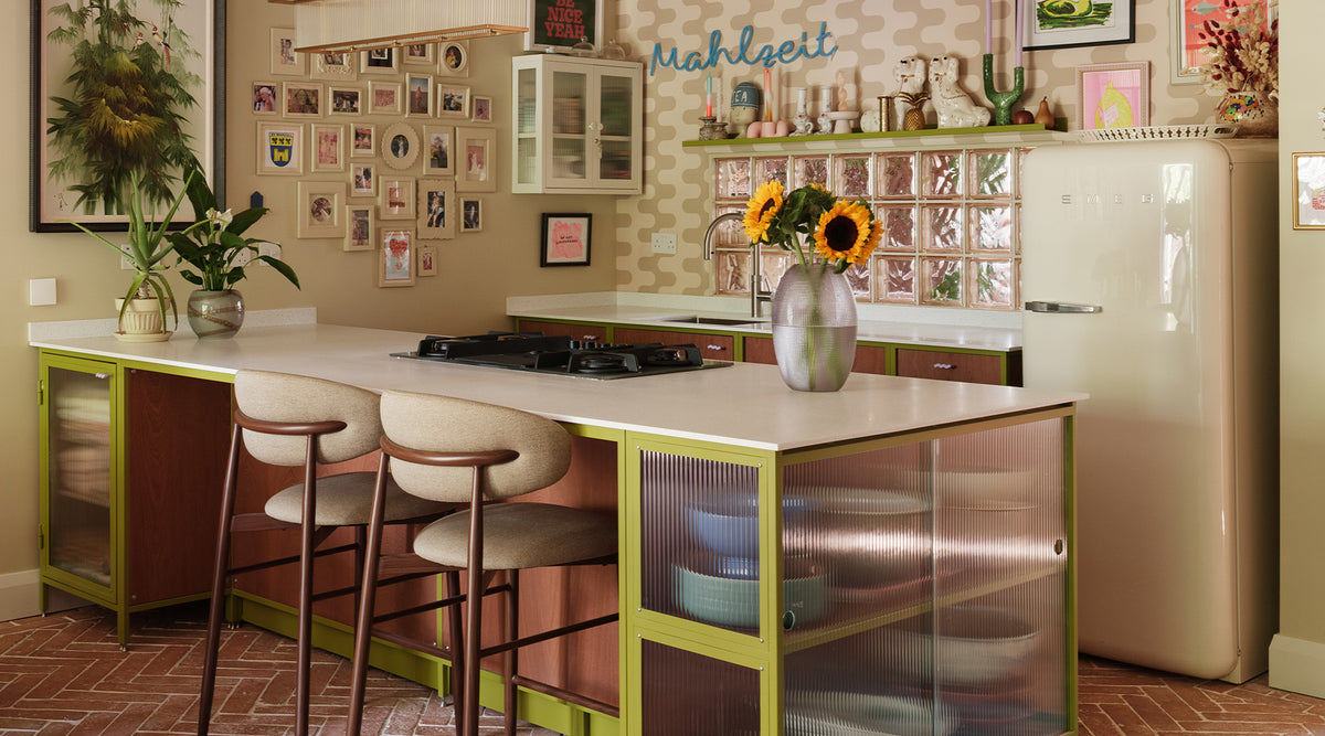 A retro-style kitchen island with a cream countertop, lime green frame, and two bar stools, set in a vintage-inspired kitchen with a cream refrigerator and tiled backsplash.